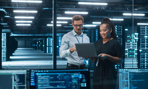 Woman and man looking at laptop surrounded by high process computers