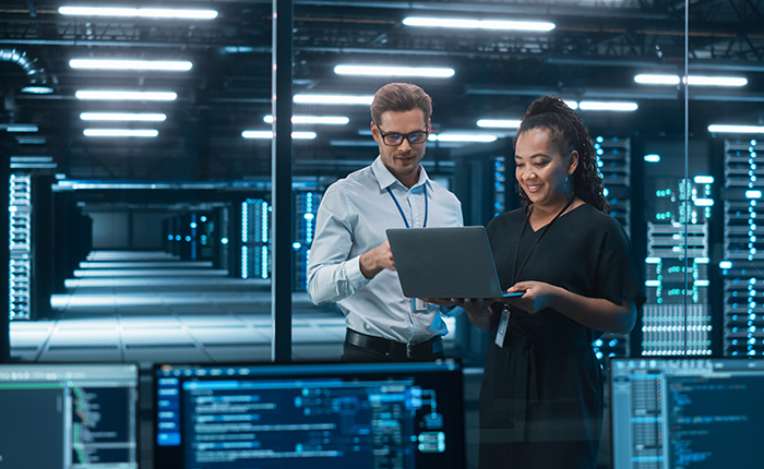 Woman and man looking at laptop surrounded by high process computers