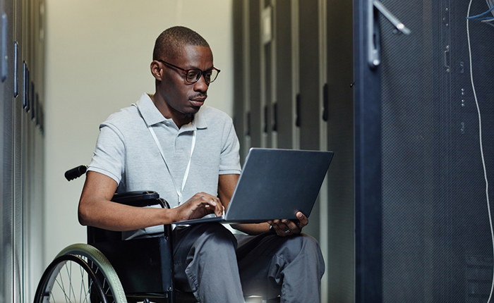 Un homme en fauteuil roulant travaillant sur un ordinateur portable dans un bureau en arrière-plan