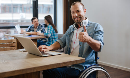 Smiling man in wheelchair giving a thumbs up working on a computer
