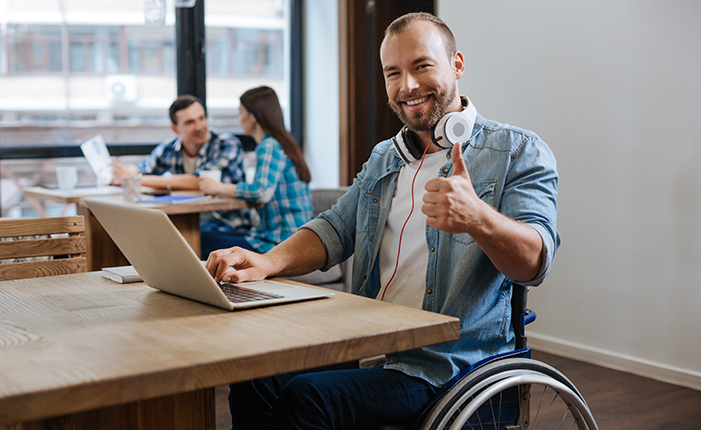 Smiling man in wheelchair giving a thumbs up working on a computer