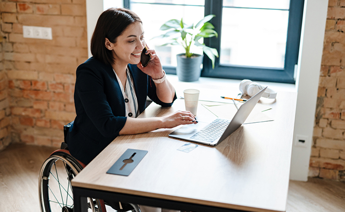 Smiling business woman talking on phone and working on laptop