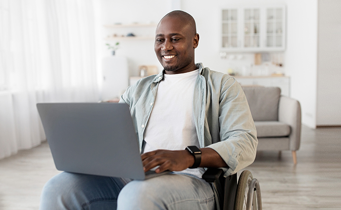 Un homme en fauteuil roulant souriant travaillant sur un ordinateur portable