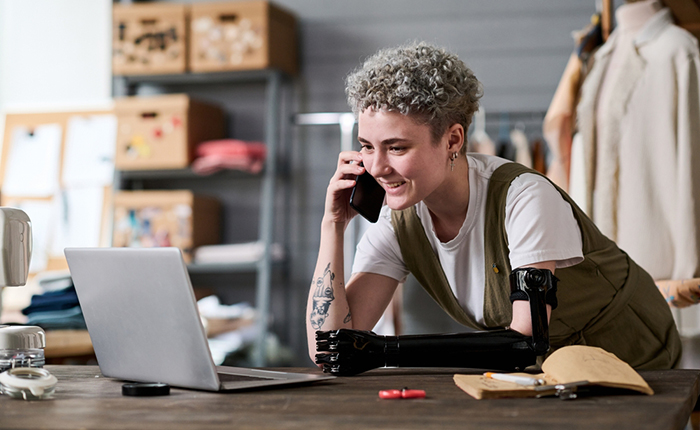 Business entrepreneur with artificial arm talking on phone while looking at a laptop