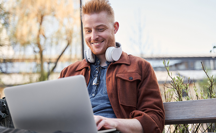 Smiling man working on laptop on a park bench