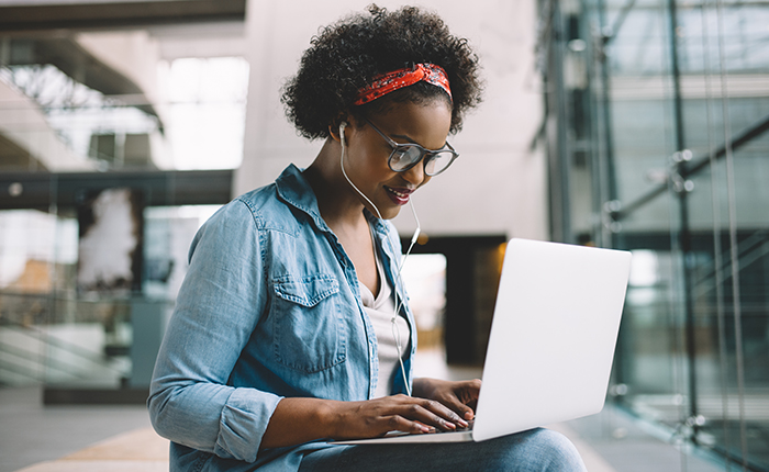 Une femme assise sur un banc, regardant un webinaire sur son ordinateur portable