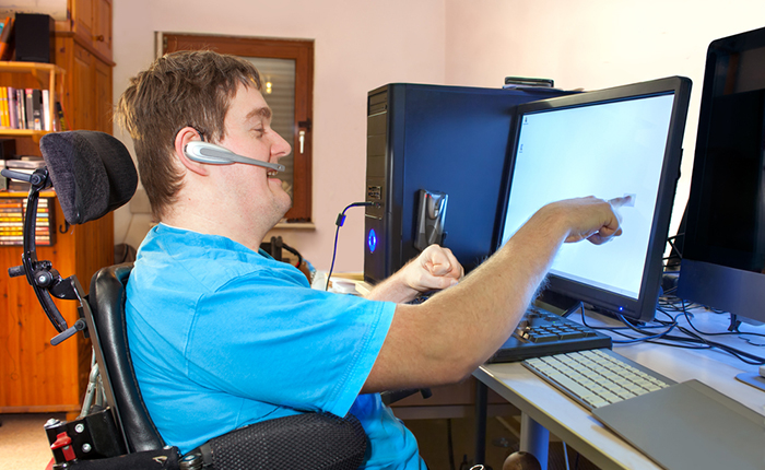 Man with disabilities in an electric wheelchair using a microphone to select SkillingUp options on a computer screen