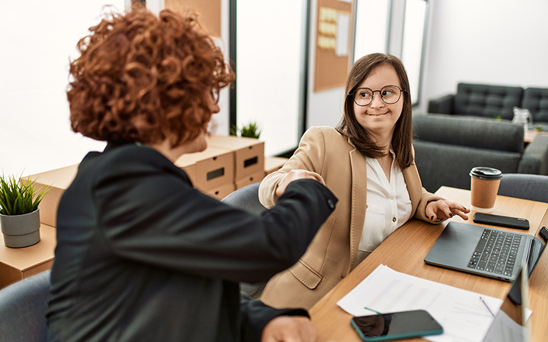 Two smiling business women, one with Down syndrome, giving each other a fist bump for success