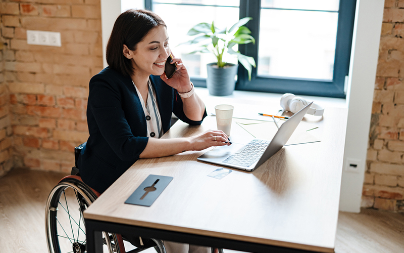 Une femme d'affaires souriante au téléphone, travaillant sur un ordinateur portable à un bureau