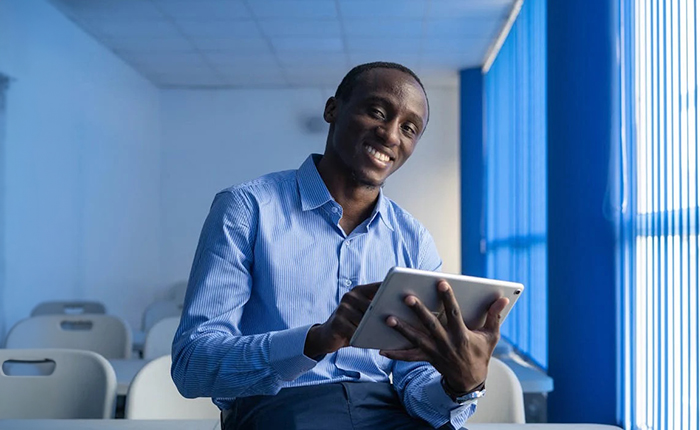 Smiling man in blue shirt sitting on a desk using a tablet